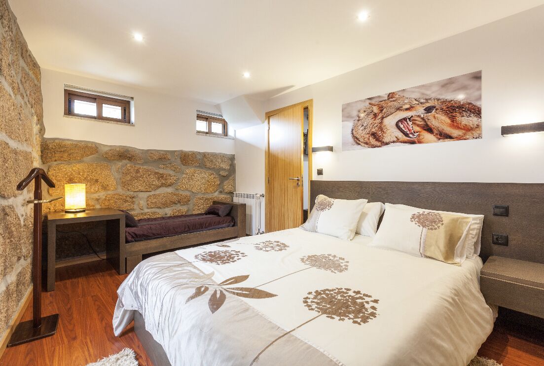 Un dormitorio con pared de piedra, cama con colcha estampada, mesita de noche con lámpara y un cuadro de un animal salvaje en la pared.