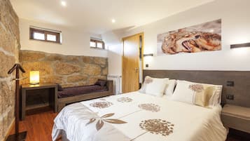 A bedroom with a stone wall, a bed with a floral bedspread, a nightstand with a lamp, and a painting of a wild animal on the wall.