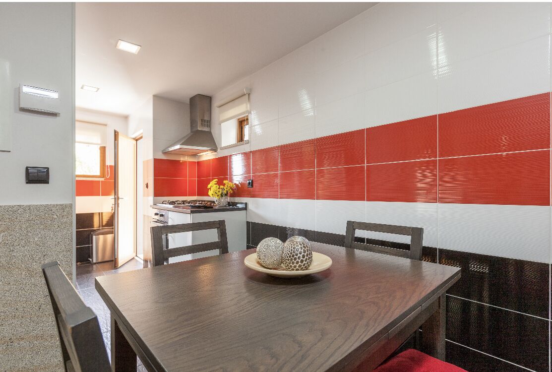Une cuisine moderne avec des carreaux rouges et blancs, une table à manger en bois et un four encastré.