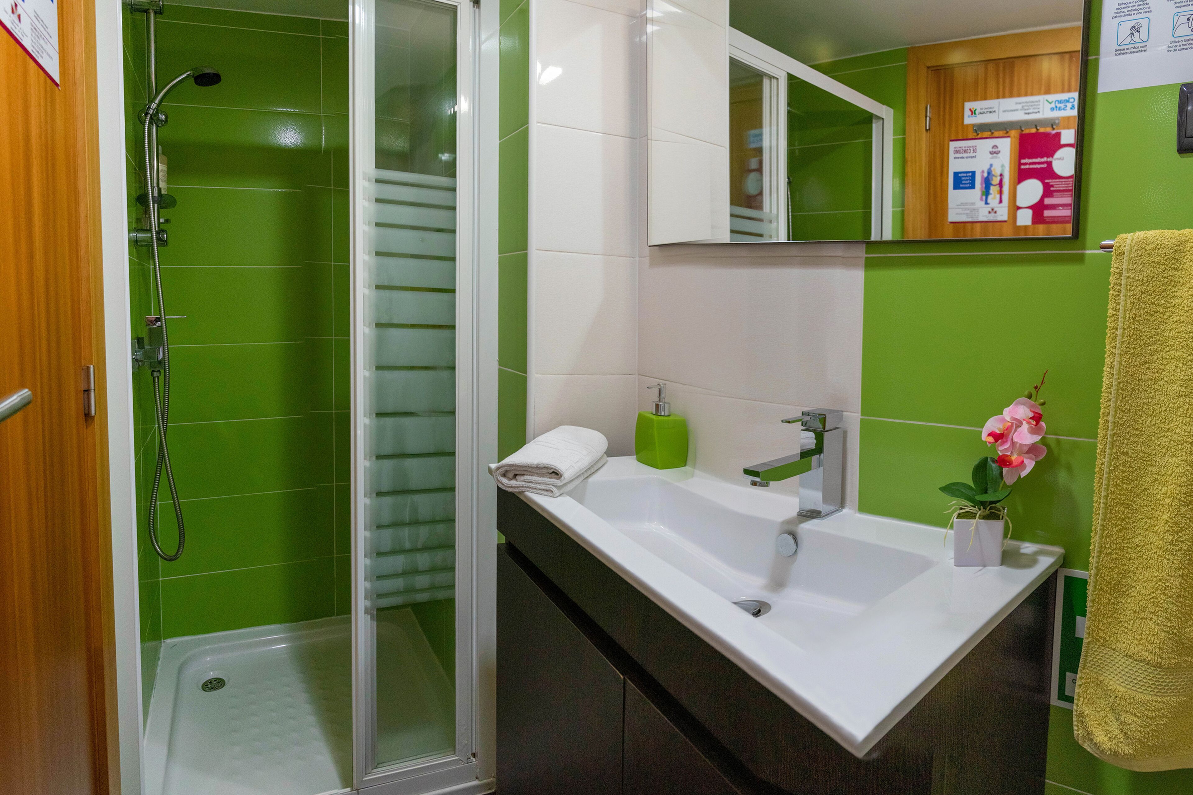 Een badkamer met een douche, wastafel, spiegel en een muur met groene tegels.