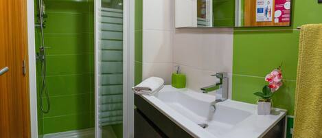 A bathroom with a shower, a sink, a mirror, and a green tiled wall.