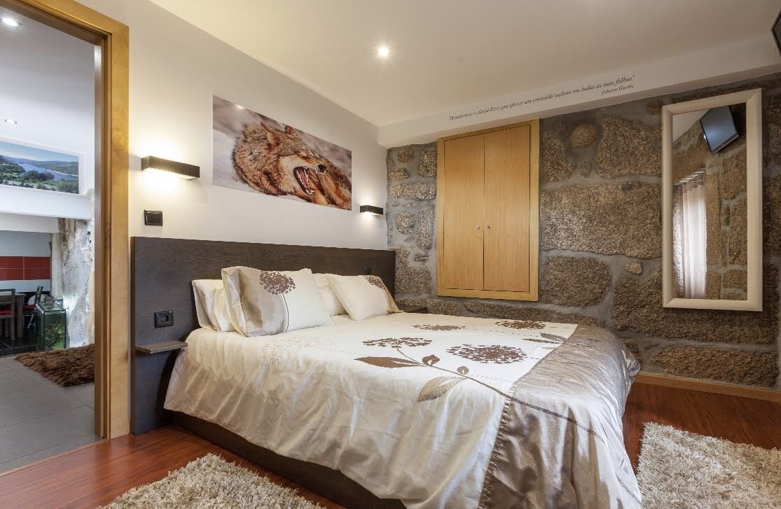 A bedroom with a large bed, a stone wall, a wooden wardrobe, and a painting of a cheetah.