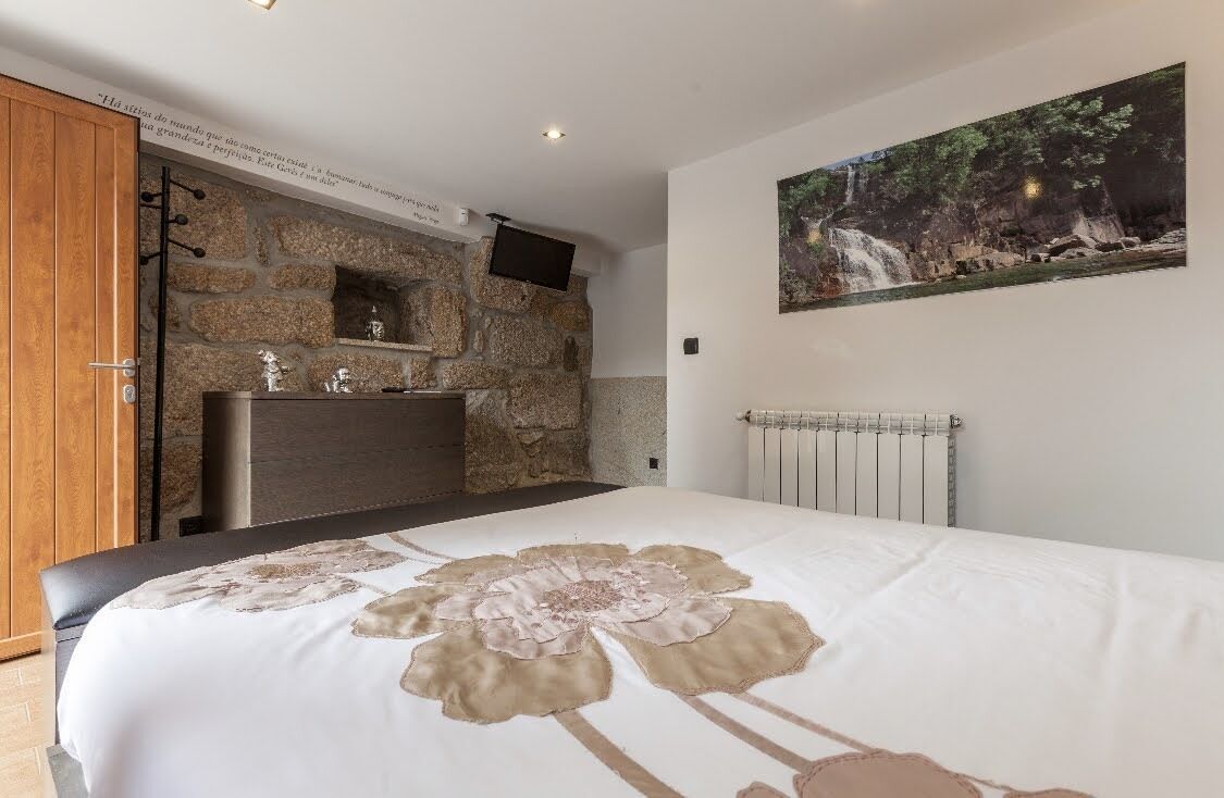 A bedroom with a stone fireplace, a bed with a floral bedspread, a mounted TV, and a waterfall painting on the wall.
