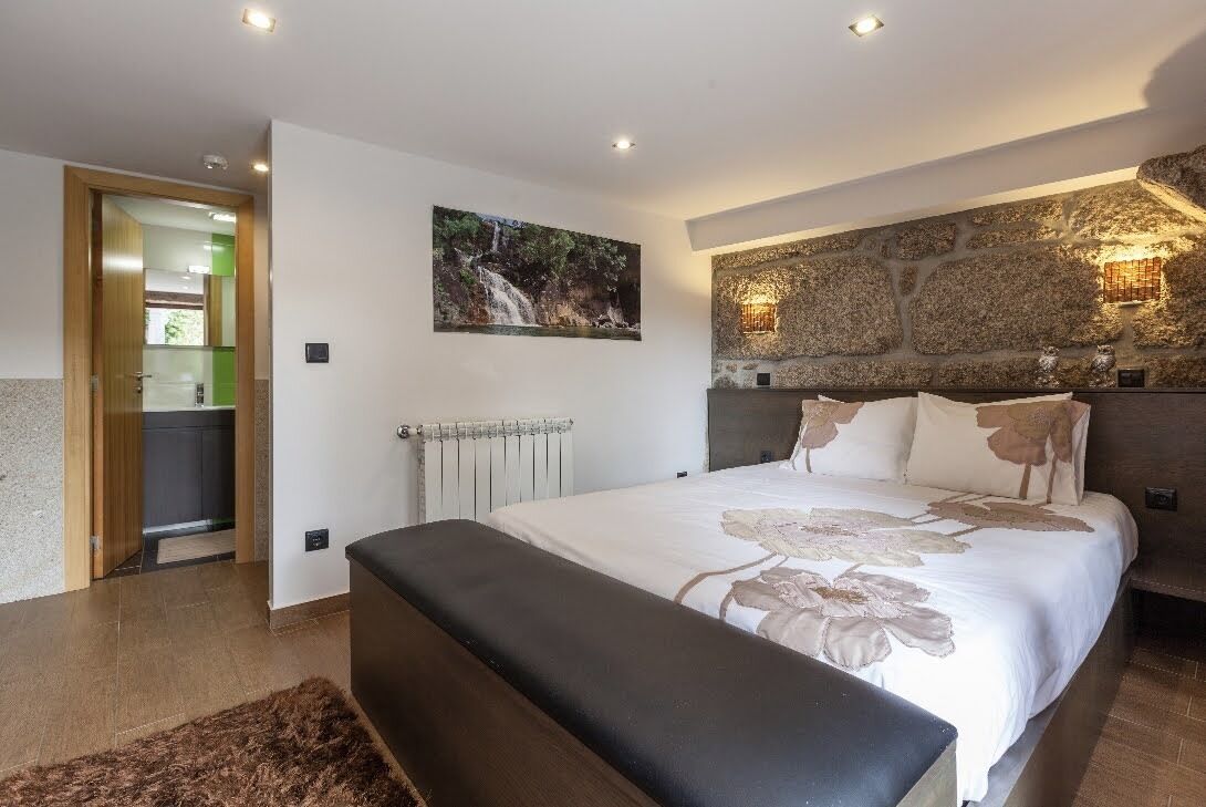 Un dormitorio con una cama grande, un banco de madera, un radiador, una pared de piedra y un cuadro de una cascada.