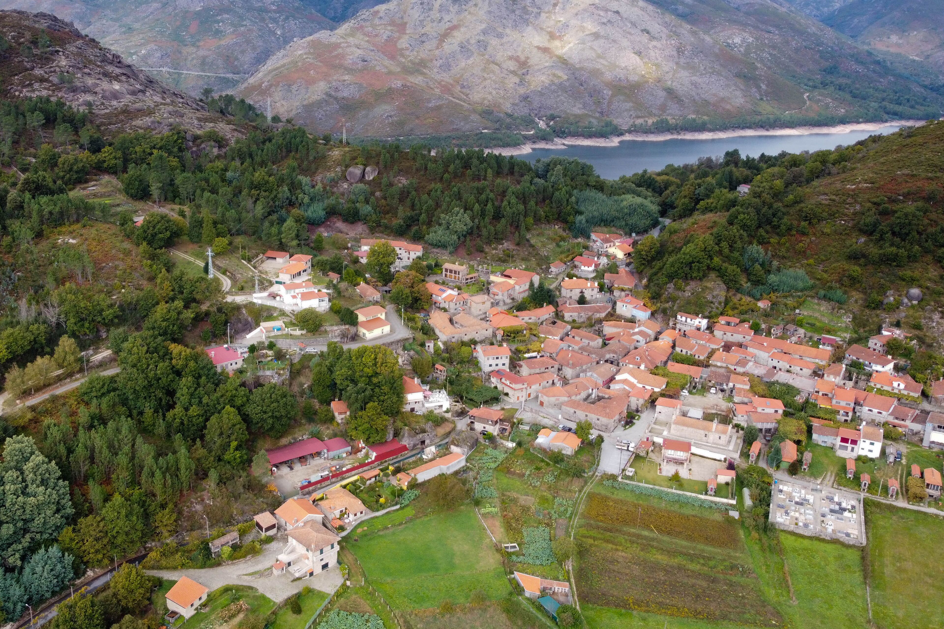 An aerial view of a village with houses, a road, and a body of water in the background.