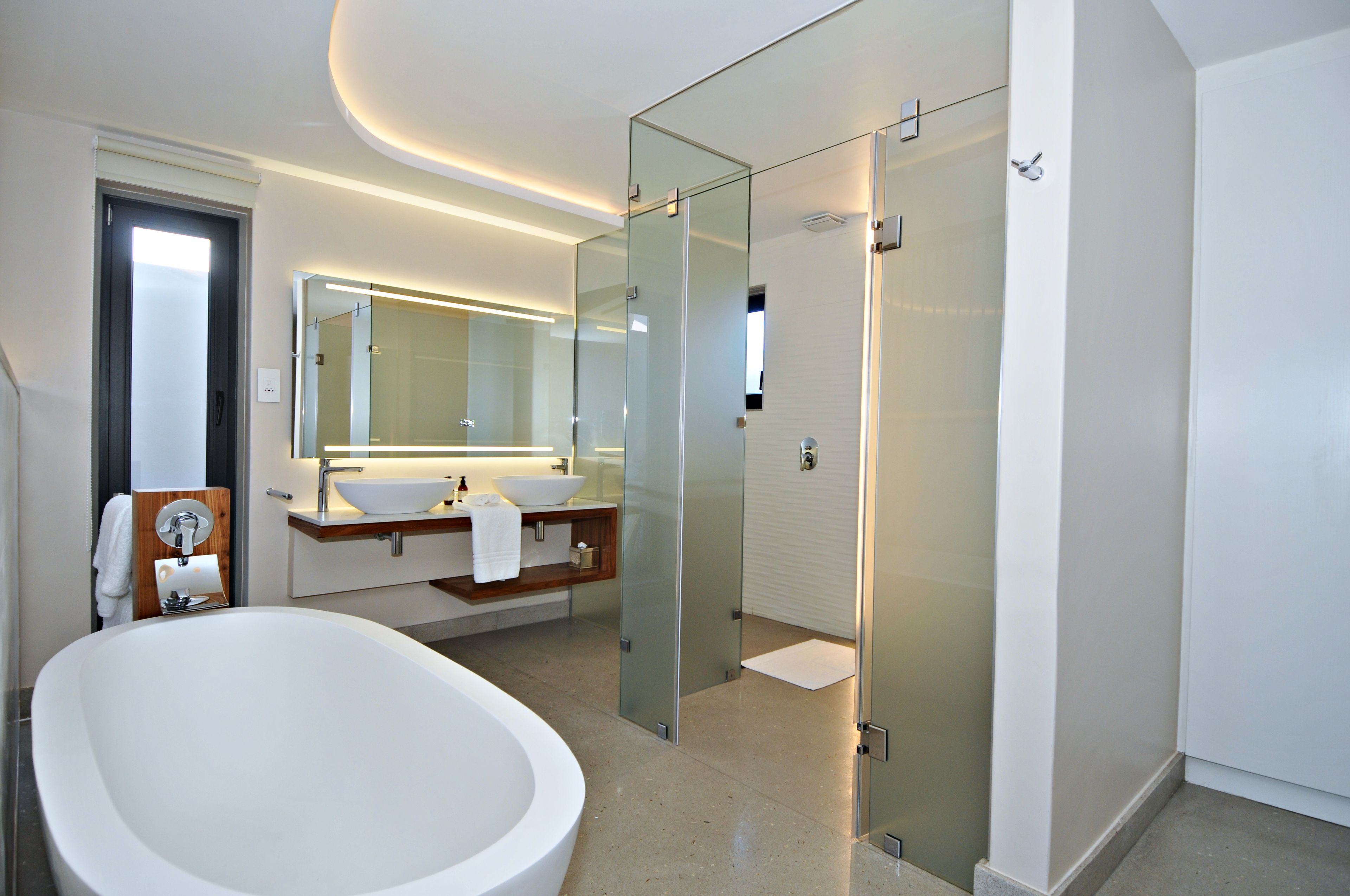 Een moderne badkamer met een vrijstaand bad, een douche met glazen wand en een grote spiegel boven de wastafel.