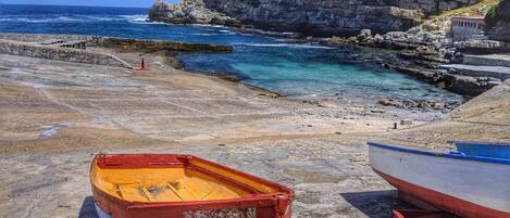 A rocky coastal area with two boats, a clear blue sky, and a rugged cliff in the background.