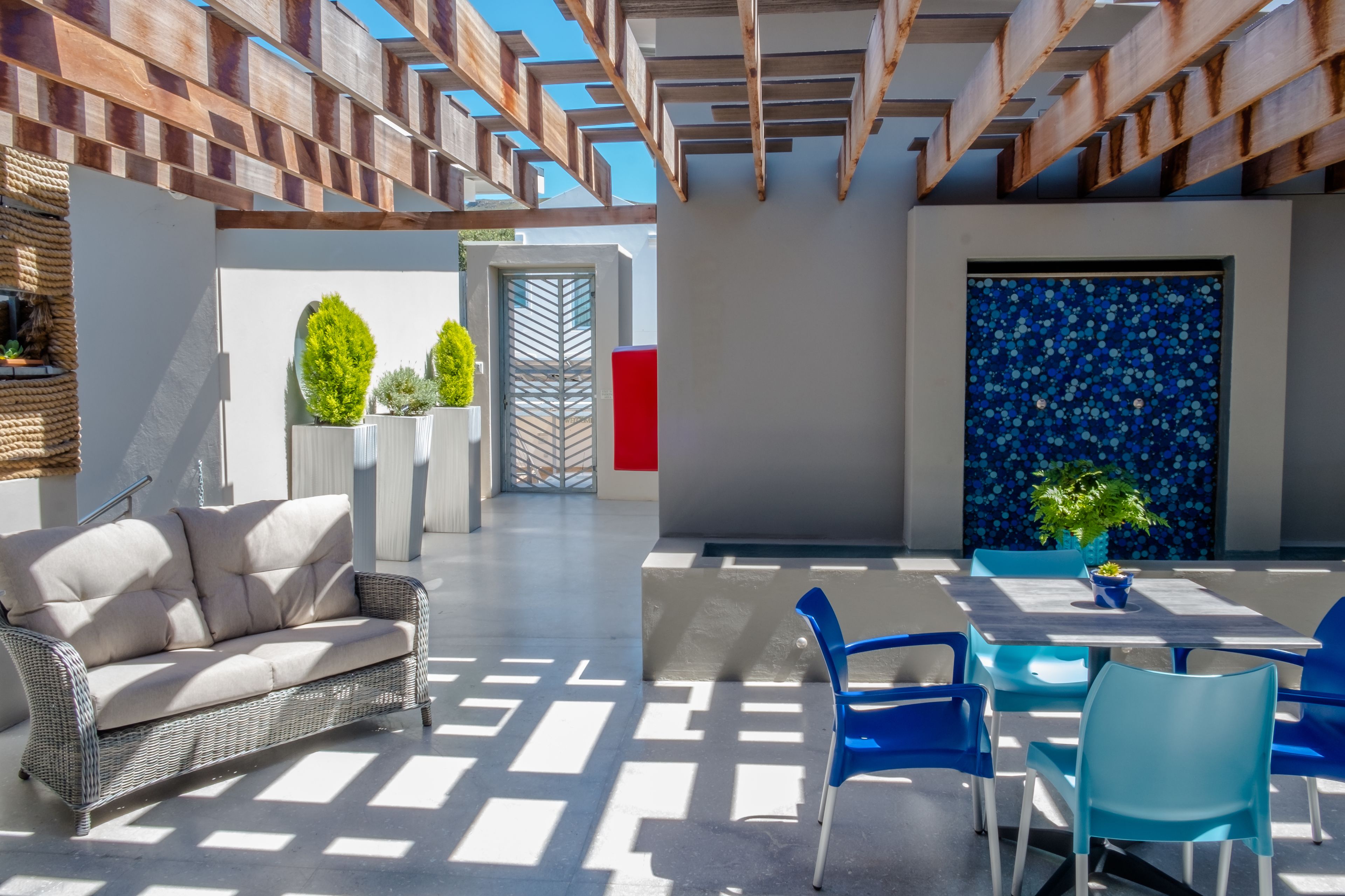 Un patio exterior moderno con un sofá de mimbre, sillas azules y una mesa de comedor.