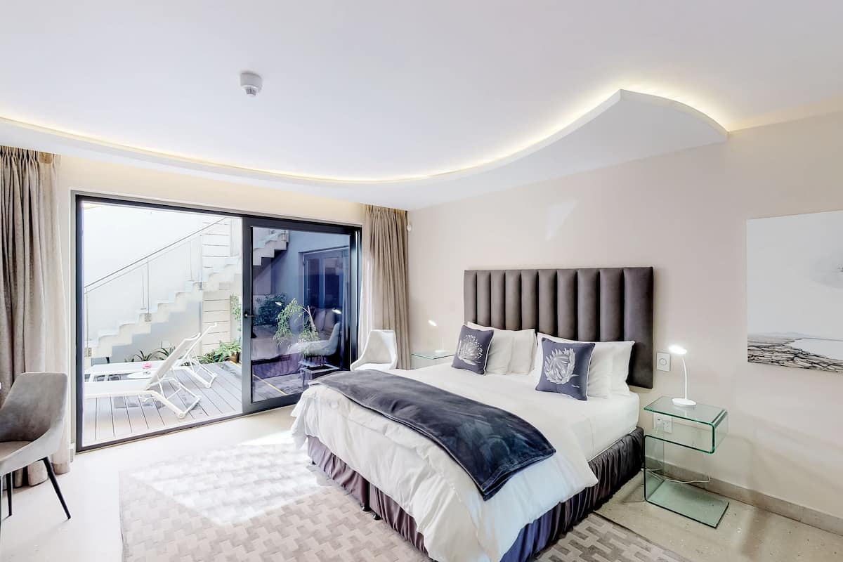 Quarto moderno com uma cama grande, porta de vidro para uma varanda e um quadro na parede.