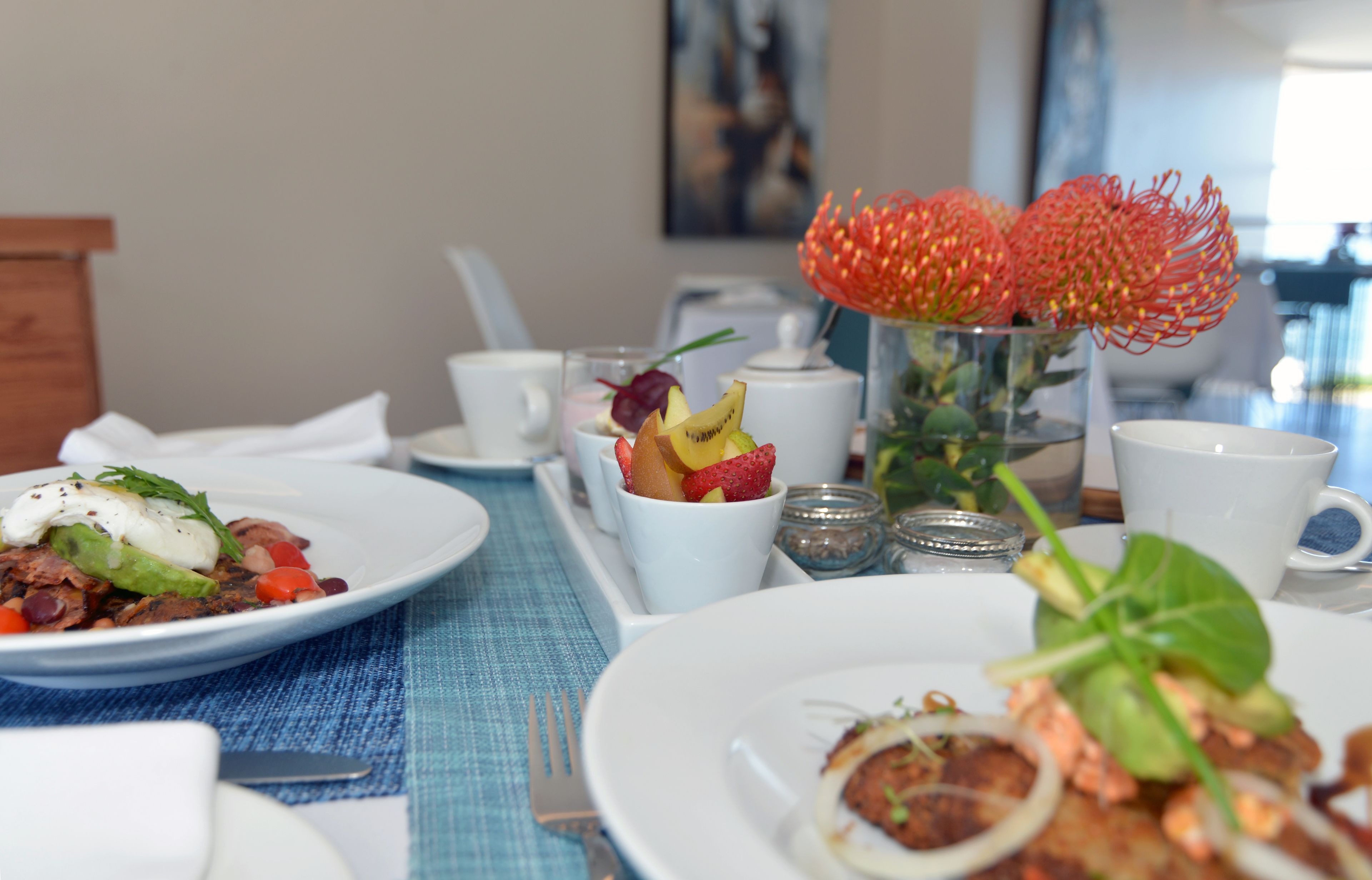 Una mesa de comedor con platos de comida, un florero con flores rojas y un cuadro en la pared.