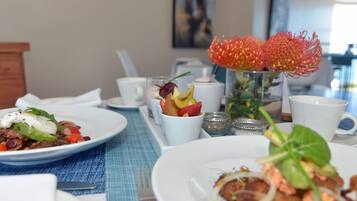 Una mesa de comedor con platos de comida, un florero con flores rojas y un cuadro en la pared.
