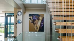 A modern interior with a glass railing, artwork on the walls, and a staircase with wooden steps.