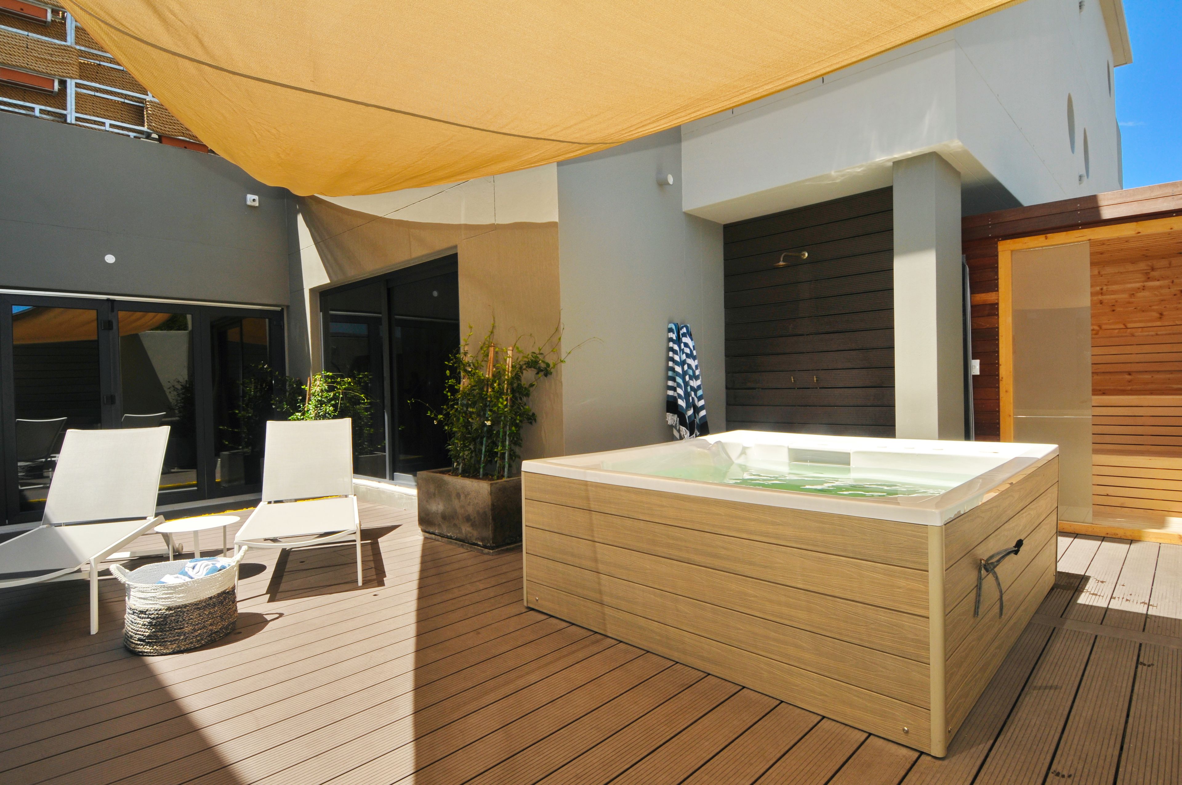 A modern outdoor area with a wooden deck, a hot tub, and two white lounge chairs.