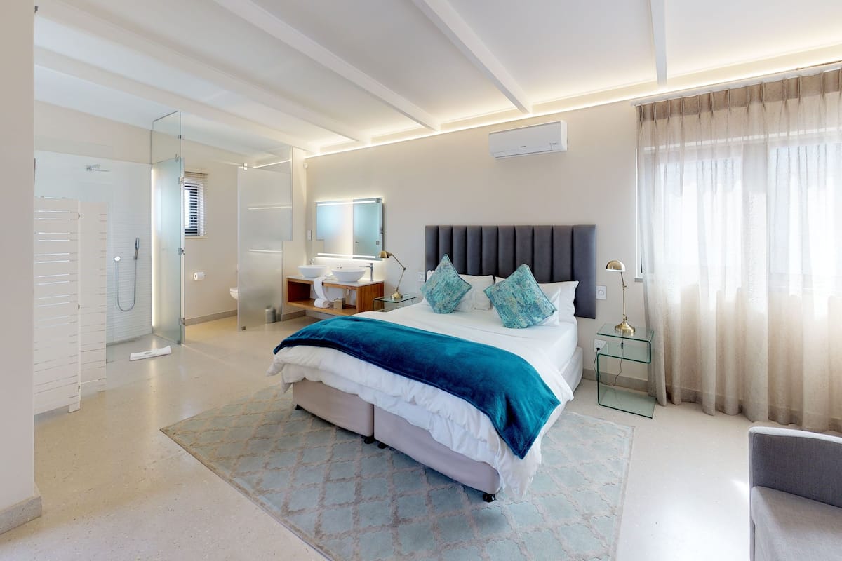 Quarto de hotel moderno com uma cama grande, uma mesa de cabeceira, um espelho e uma janela com cortinas.