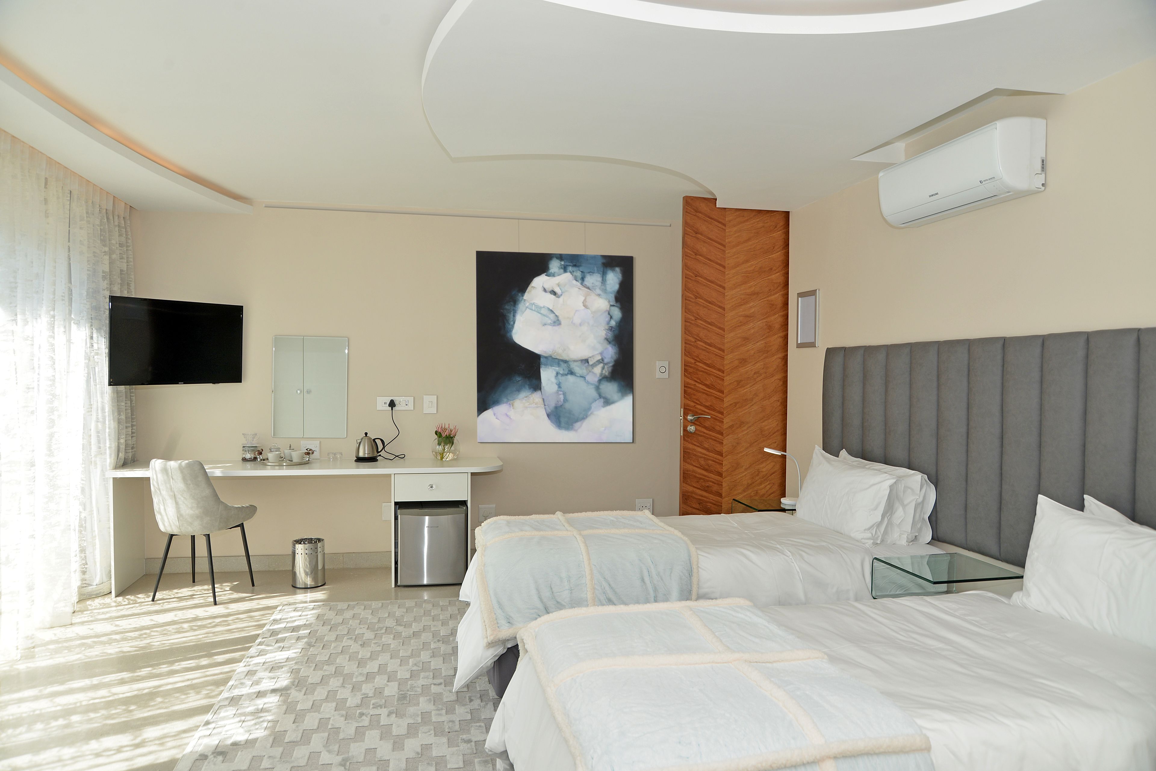 A modern hotel room with two beds, a desk, a TV, and a painting on the wall.