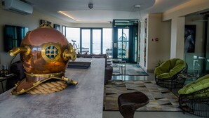 A modern interior with a large, metallic, octopus-like sculpture on a table, large windows offering a view of the sea, and contemporary furniture.