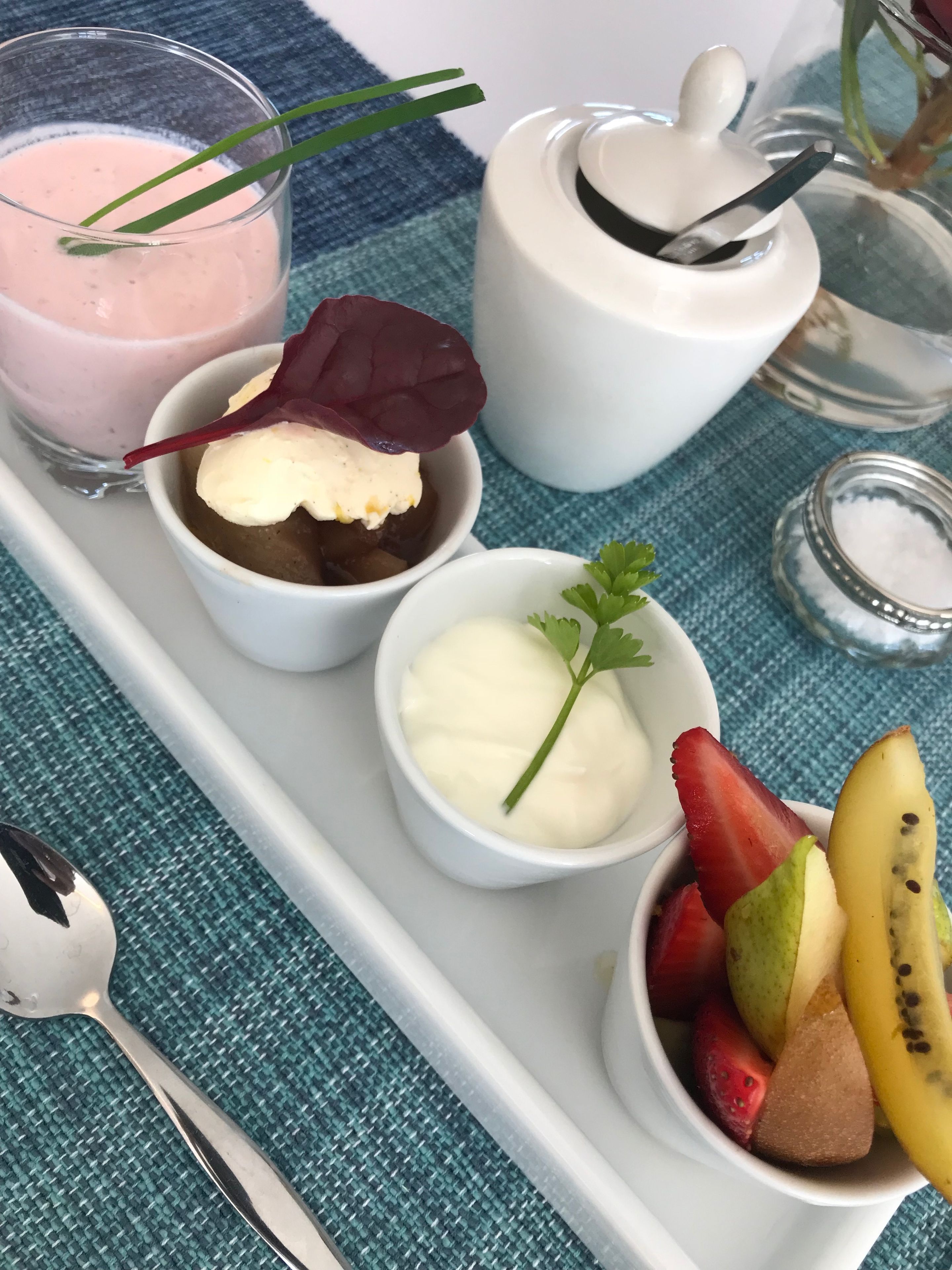 Een dienblad met een roze smoothie, een ijsje met een blad, een klein schaaltje slagroom en een schaal vol gemengd fruit.
