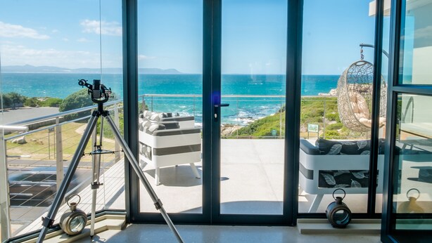 A modern room with a large glass door leading to a balcony with a view of the sea and a hanging chair.