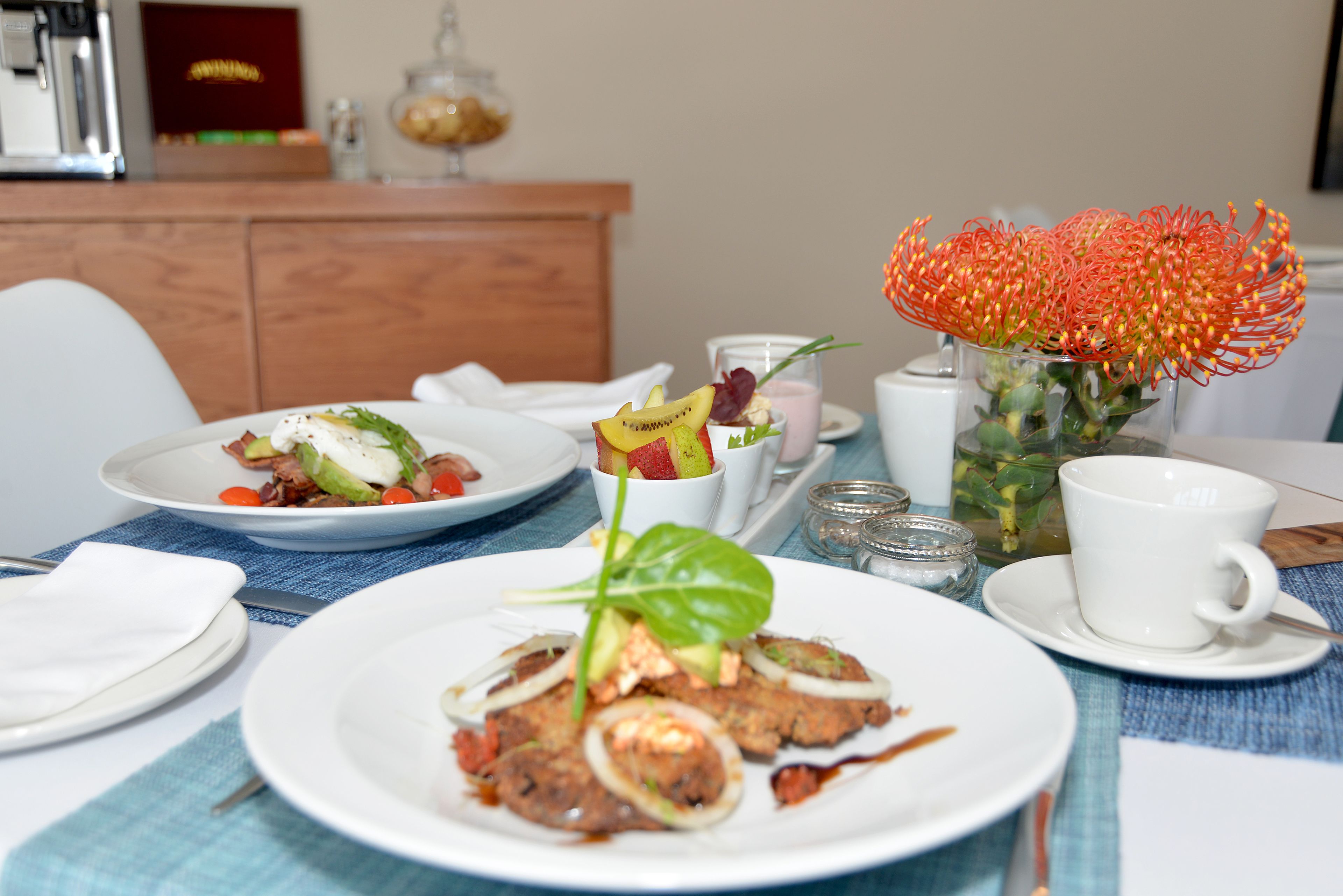 Une table à manger avec des assiettes remplies de nourriture, une tasse et un vase de fleurs.