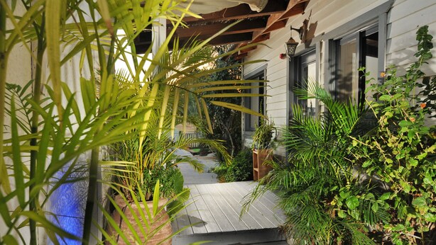 Una terraza de madera que conduce a una casa con porche cubierto, rodeada de exuberante follaje y plantas en macetas.