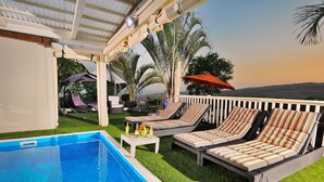 Un área junto a la piscina con tumbonas y una pérgola.