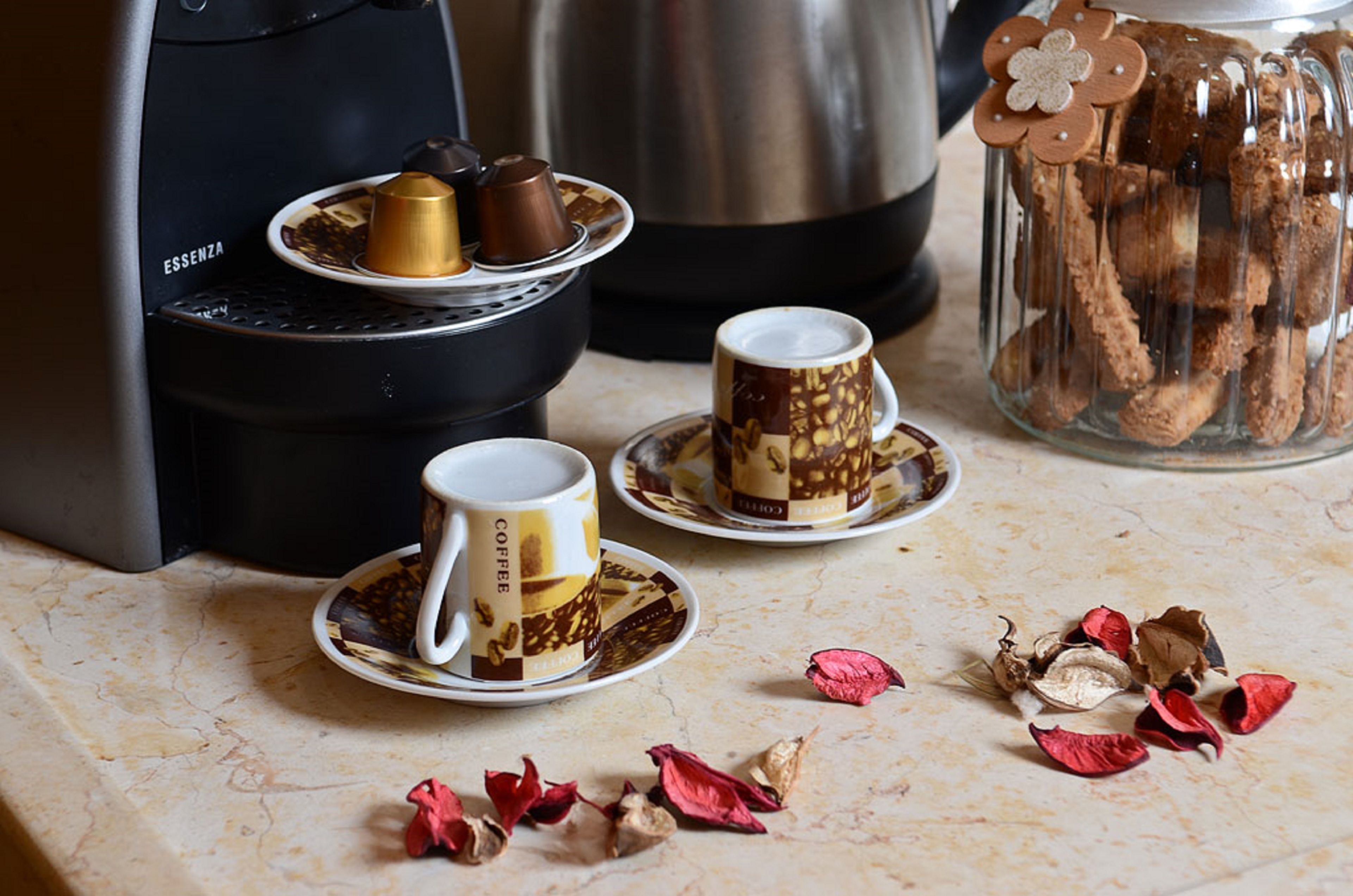 A coffee machine, two coffee cups, a plate with two chocolate cups, and a glass jar with cookies.