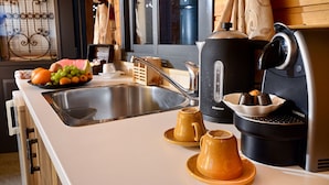 Una cocina con un lavamanos, una cafetera y un frutero.