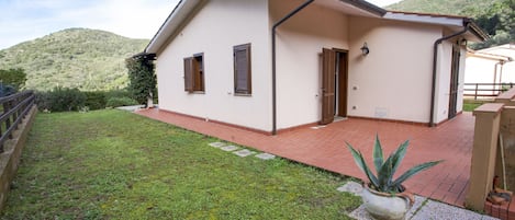 Uma casa térrea com telhado inclinado, varanda frontal e um pequeno jardim.