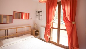 Un dormitorio con cama, cabecera de madera, mesita de noche, espejo, ventana con cortinas naranjas y un radiador.