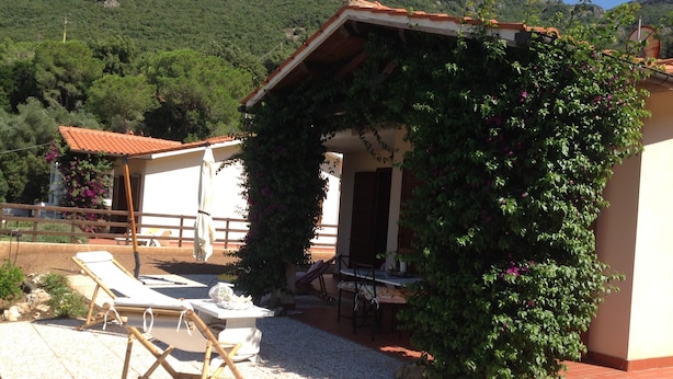 Una villa con zona de estar exterior cubierta, piscina y montañas al fondo.