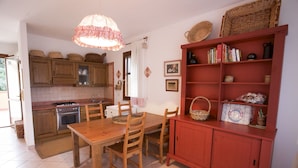 Una cocina con armarios de madera, una mesa de comedor, sillas, una estantería roja y un colgador de luces.