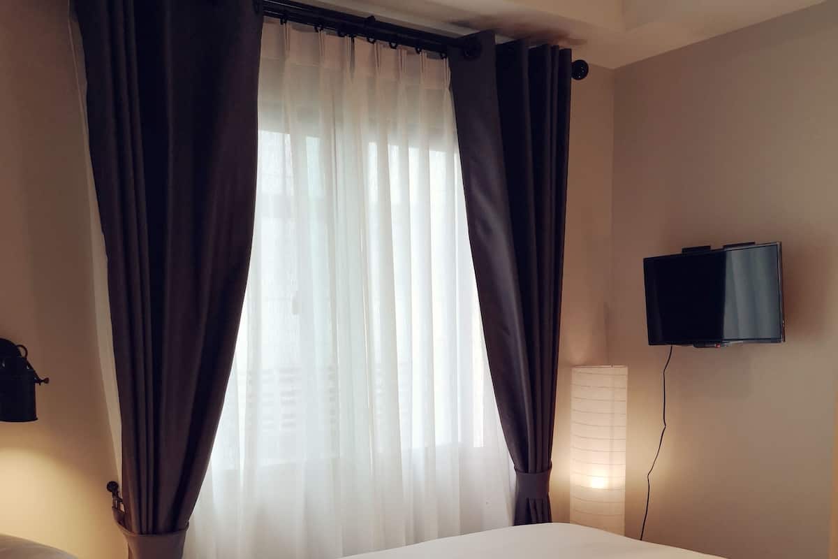 Una habitación de hotel con cama, cortinas, televisor y lámpara.