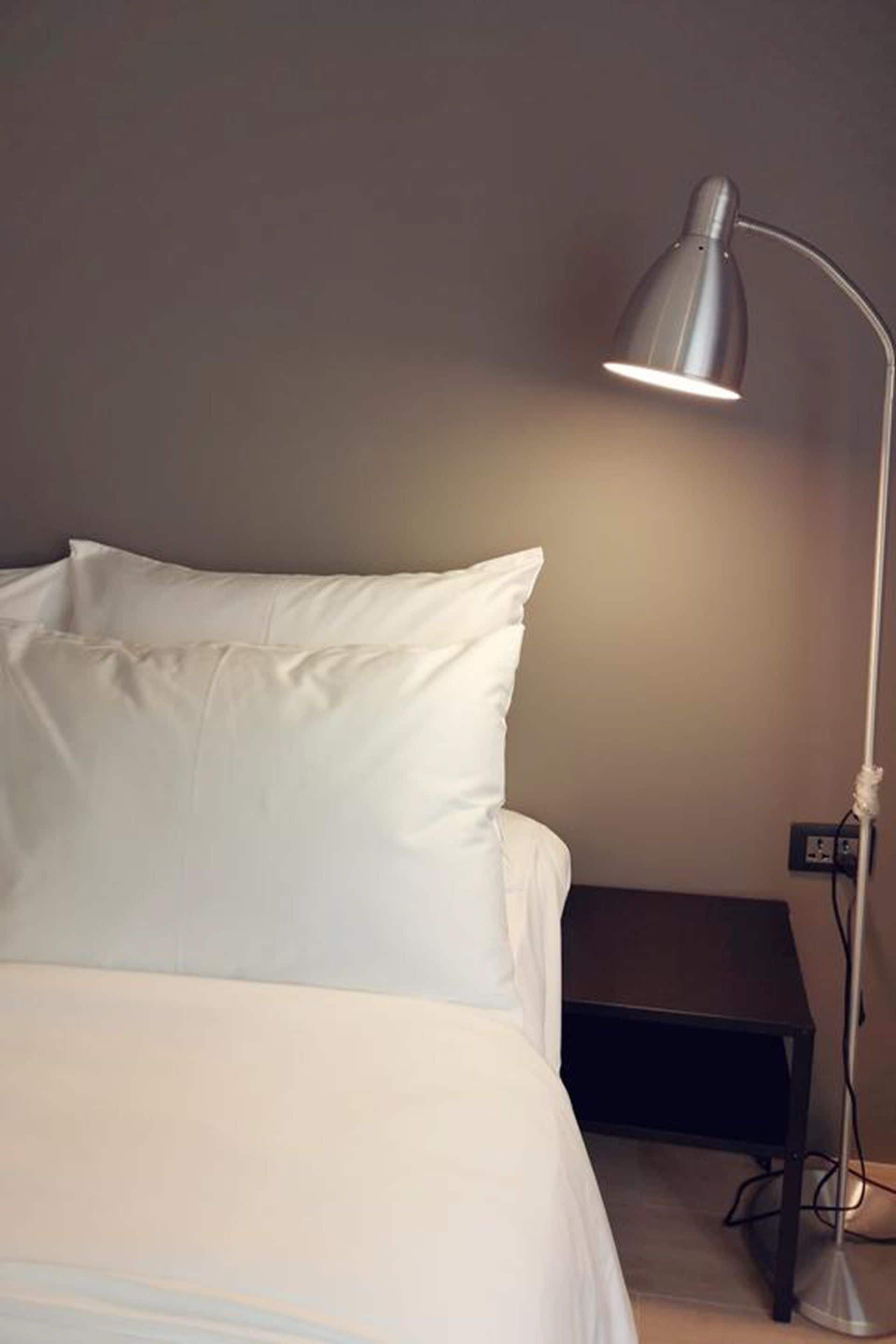 A neatly made bed with white linens, a bedside table, and a floor lamp.