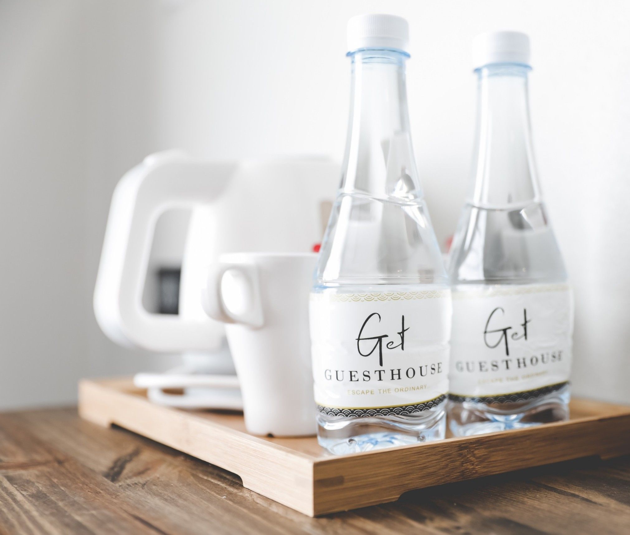 Two bottles labeled "Get Guesthouse" on a wooden tray with a white mug and a white coffee maker in the background.