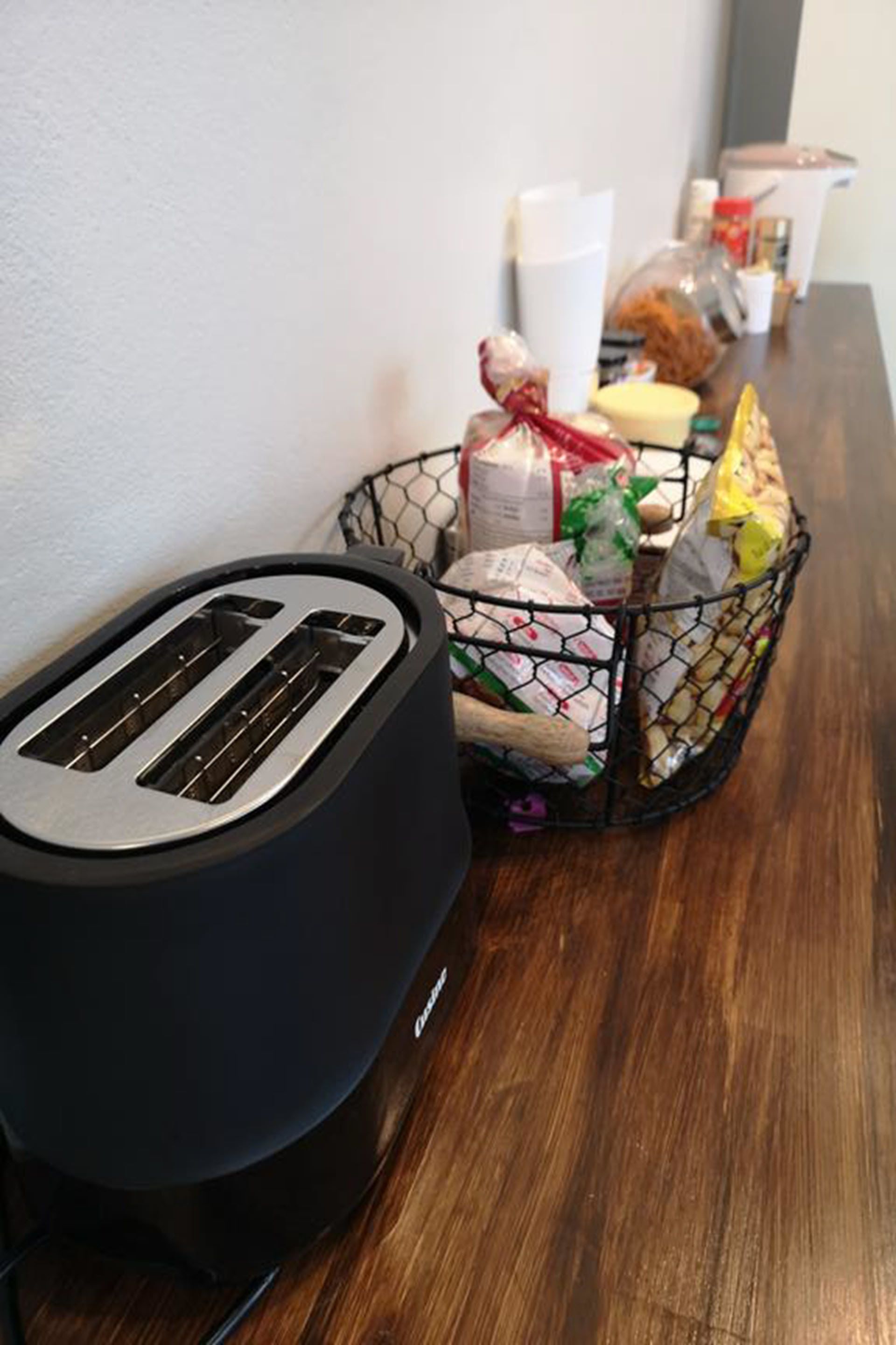 A kitchen counter with a toaster and a basket containing various food items.