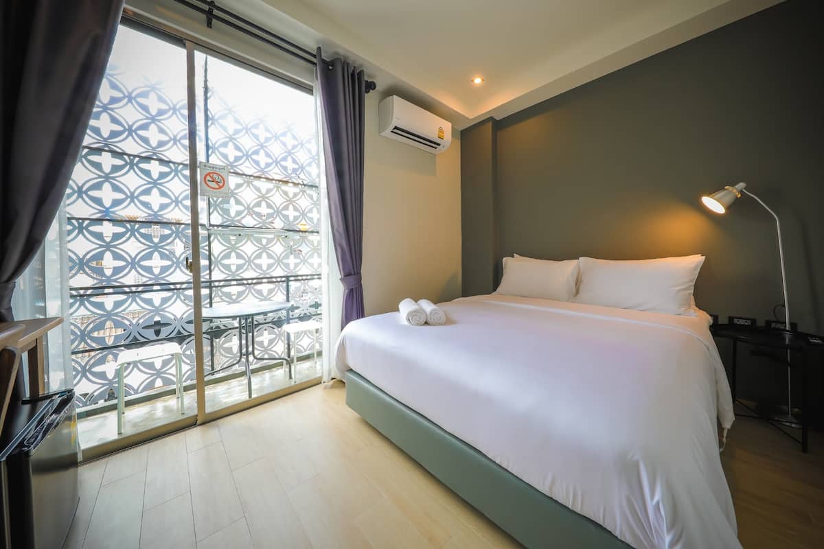 Habitación de hotel con cama, escritorio, silla y balcón con baranda ornamentada, además de un equipo de aire acondicionado.