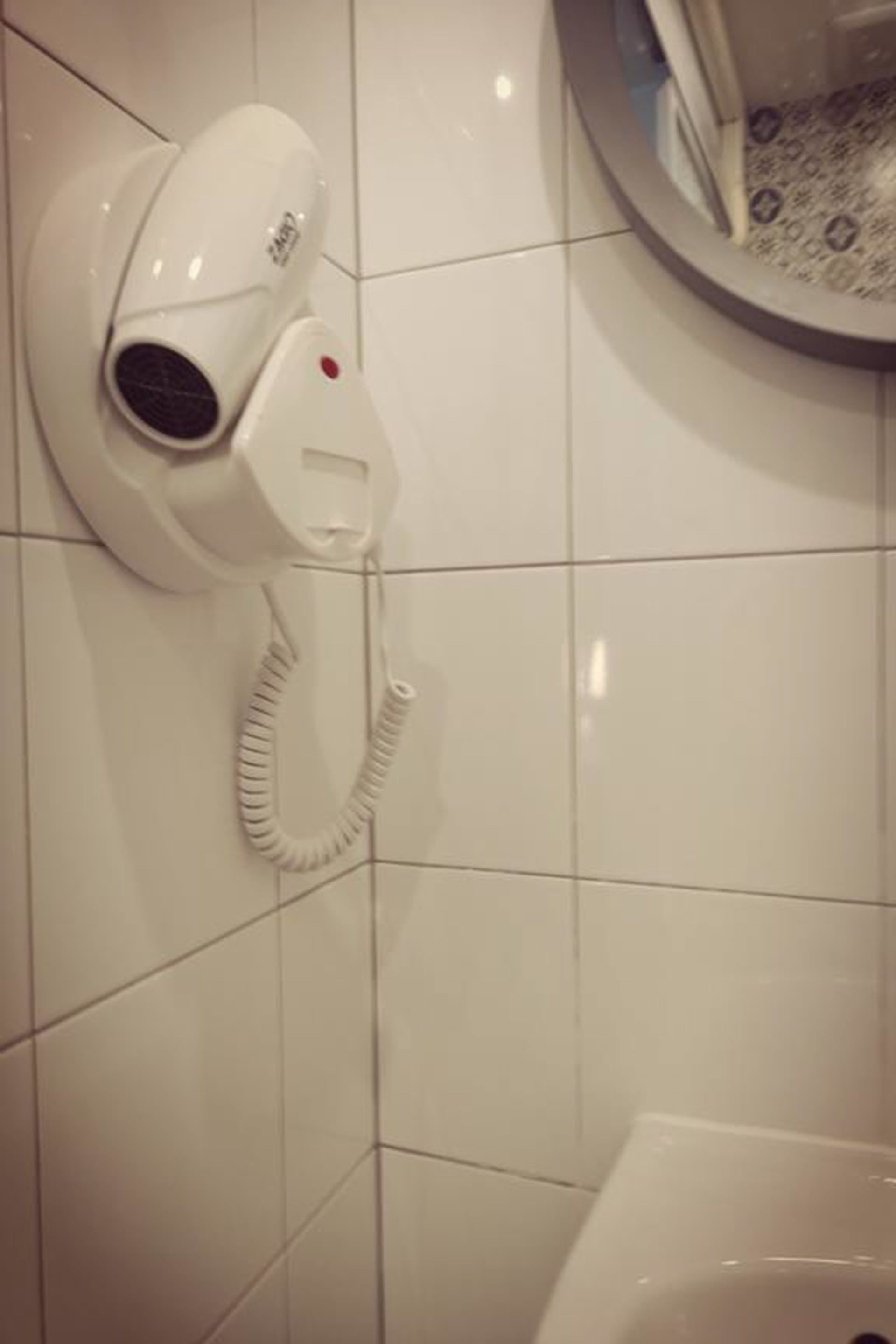 Un sèche-cheveux blanc fixé au mur, qui est recouvert de carreaux, dans une salle de bain.