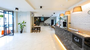 A modern hotel lobby with a marble reception desk, a staircase, and a dining area. - Get GuestHouse 2 (Hat Yai)