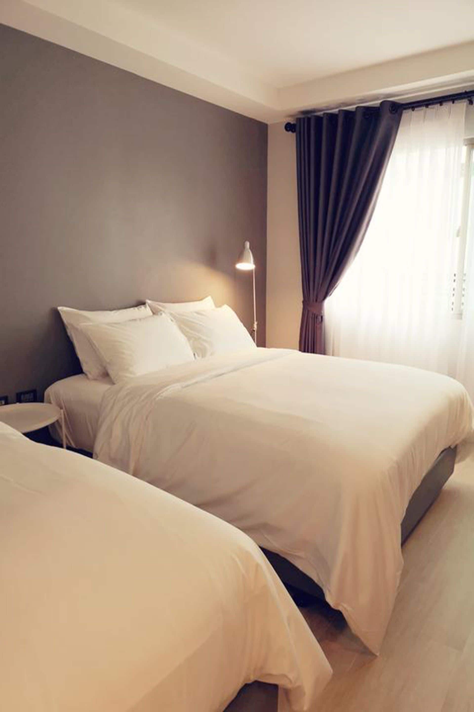Une chambre d’hôtel avec deux lits, une table de chevet, une lampe et une fenêtre avec des rideaux.