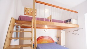 Habitación con literas, una escalera de madera, cabecera con diseño de sol y colcha azul.