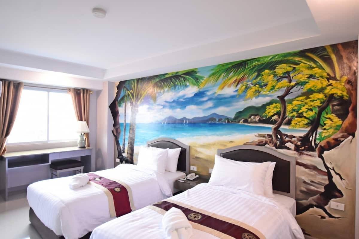 A hotel room with two beds, a desk, and a large beach mural on the wall.