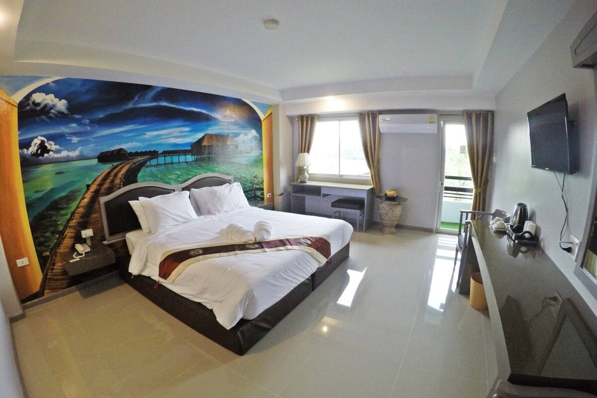A hotel room with a large bed, a desk, a TV, and a mural on the wall.