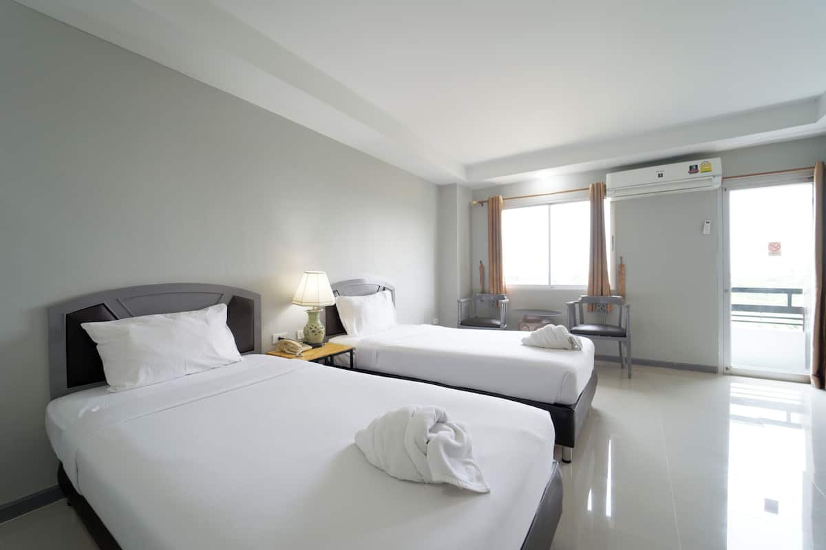 A hotel room with two beds, a desk with a lamp, a chair, and a window with curtains.