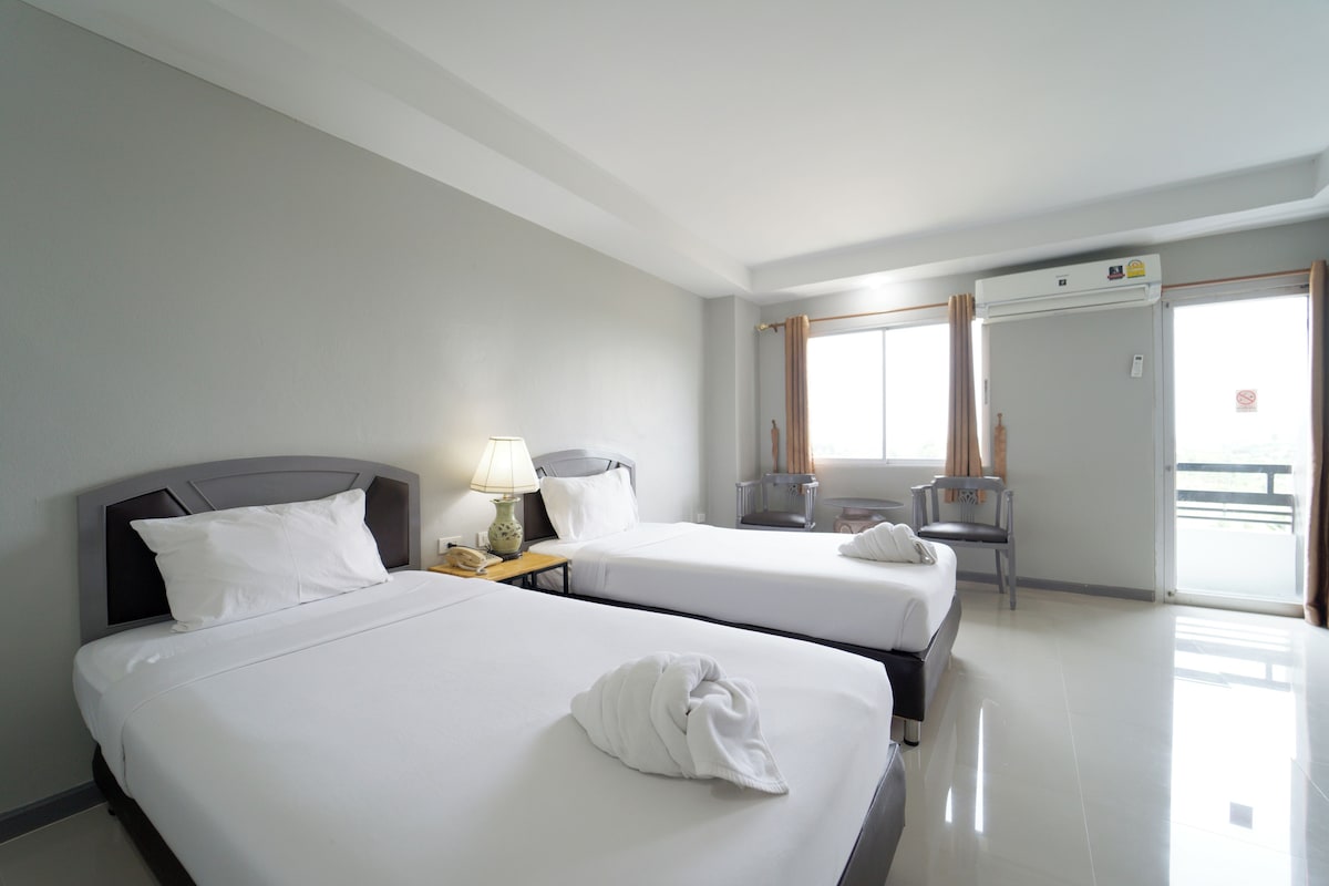 A hotel room with two beds, a desk with a lamp, a chair, and a window with curtains.