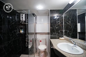 A modern bathroom with a glass-enclosed shower, a white sink, and a large mirror. - Bcp Hotel Rayong (Ban Chang)