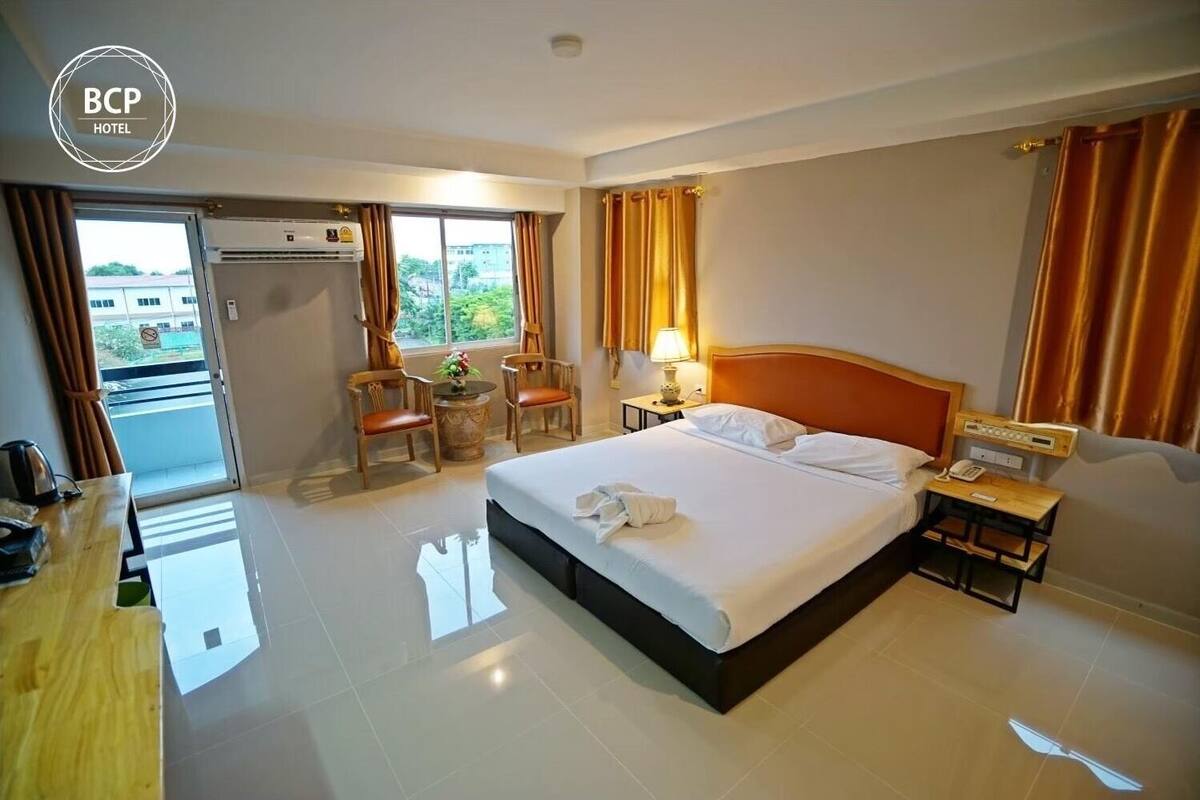 A hotel room with a bed, two chairs, a small table, a nightstand, and a window with curtains.