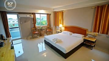 Una habitación de hotel con cama, dos sillas, una mesita, una mesita de noche y una ventana con cortinas.