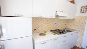 A kitchen with white cabinets, a gas stove, and a sink. - Appartamento Il Maretto (Capoliveri)