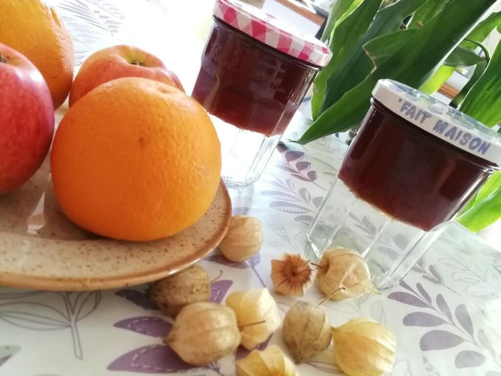 A table with fruits, jars of jam, and a glass of juice.