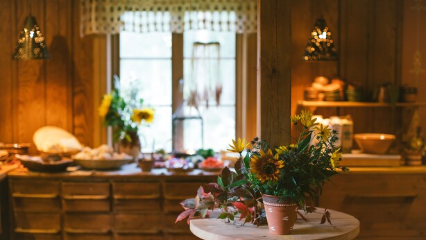 Una cocina rústica con armarios de madera, una mesa redonda de madera y una planta en maceta, además de un ventanal con vistas al exterior.